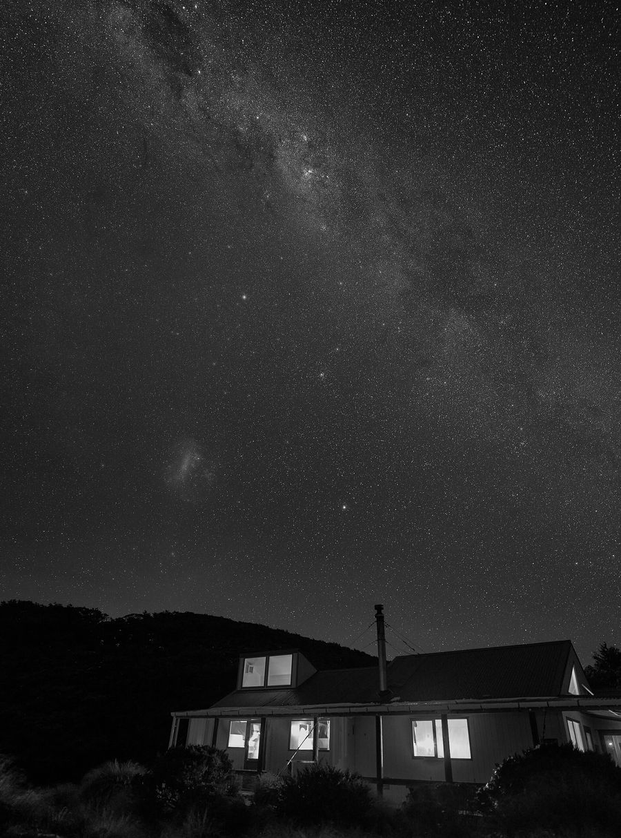 Sunrise Hut in the Ruahine Range at night, its windows lit, under the Milky Way