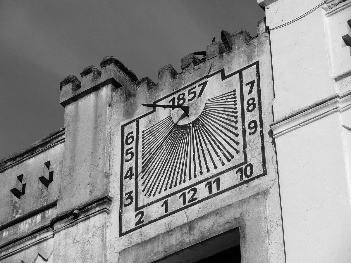 A wall sundial dated 1857 in Curitiba, Brazil: an iron gnomon casts its shadow across painted hour lines.